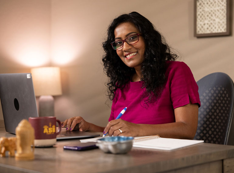 ASU alumna working at a desk with a laptop and notebook.