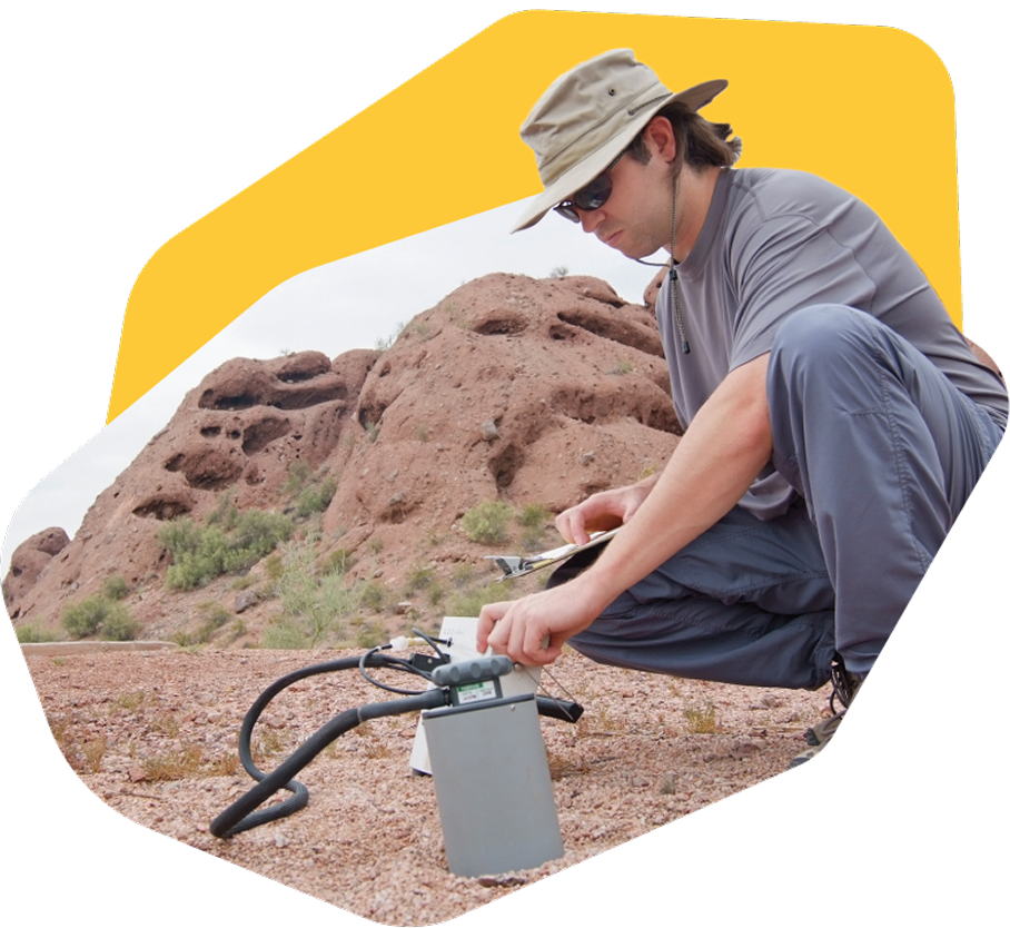 Researcher using field equipment on rocky desert terrain.